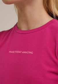 Fuchsiové tričko s krátkým rukávem a kulatým výstřihem, na kterém je nápis "UDĚLEJ DNEŠEK ÚŽASNÝM" v jemně růžové barvě, vyrobené z měkké bavlny.