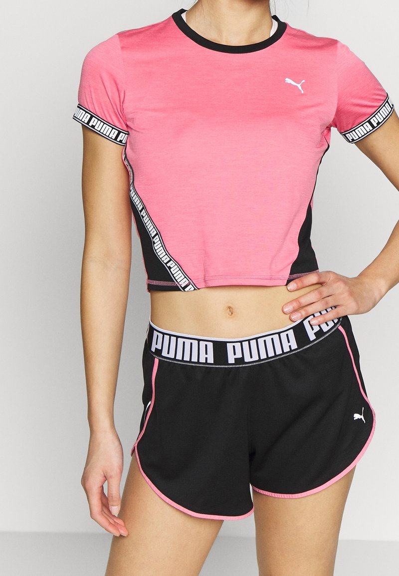 Rosa kortärmad sportt-shirt med svarta accenter och Puma-logotyp, tillsammans med svarta shorts med rosa detaljer och en logotypmärkt midja.