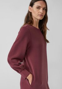 Bordeauxfarbendes Sweatkleid mit langen, puffigen Ärmeln, rundem Ausschnitt und Seitentaschen. Sanfte Textur mit lockerer Passform und minimalistischem Design.