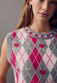 Knit sleeveless sweater featuring a diamond pattern in gray, pink, and white, with a heart accent and a colorful ribbed neckline.