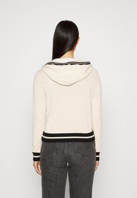 Sweat à capuche beige clair avec un col rayé noir et blanc et un ourlet côtelé. Confectionné en tissu doux, il présente une coupe décontractée et des manches longues.