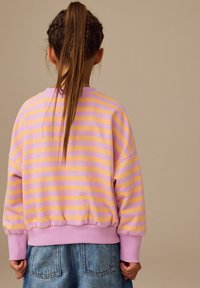 Lila och gulrandig sweatshirt med ribbat avslut, lös passform och korta ärmar, kombinerad med ljusa denimshorts.