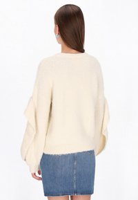 Kremowy puszysty sweter z balonowymi rękawami, zestawiony z dżinsową spódnicą. Sweter ma prążkowany dół i miękką teksturę.