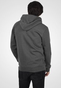 Grijze hoodie met een relaxte pasvorm, voorzak in kangoeroestijl en ribgebreide mouwen, gedragen over donkere jeans, gezien vanaf de achterkant.