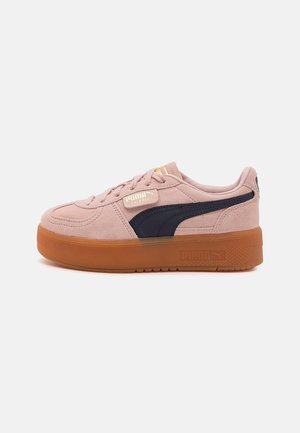 Różowe zamszowe buty sportowe Puma Palermo z czarnym paskiem i grubą brązową gumową podeszwą, widziane z boku na białym tle.
