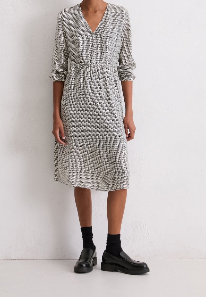 Personne portant une robe mi-longue à manches longues avec un petit motif en zigzag noir, associée à des chaussettes noires et des mocassins à plateforme noirs.