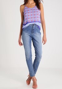 Modrý top na ramínka s potiskem, kombinovaný s vysokými světle modrými džíny a růžovými sandály na podpatku. Hladká tkanina.