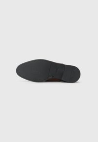 Black rubber sole of a shoe with a smooth texture. The underside features a logo and subtle design details. The edges are curved and contoured.