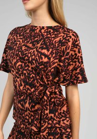 Haut à encolure arrondie, manches courtes, avec un détail noué sur le côté, présentant un motif abstrait audacieux en noir et orange sur un tissu doux.