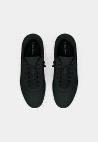 Μαύρα casual αθλητικά παπούτσια με λείο επάνω μέρος από ύφασμα, κορδόνια τόνου, και λευκές λαστιχένιες σόλες με διακριτικές οπές και λεπτομέρειες επωνυμίας.