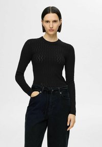 Zwarte, langärmige, aansluitende top met een gestructureerd ruitpatroon, gecombineerd met donkere denim high-waisted broek met een strikceintuur en zijzakken.