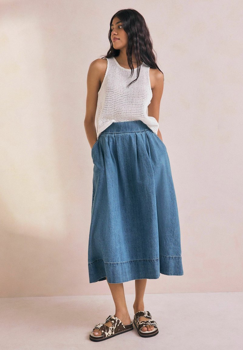 Vit stickad linne topp som matchas med en lång blå denimkjol med en rynkad midja. Bruna sandaler med mönster av nötkreatur.