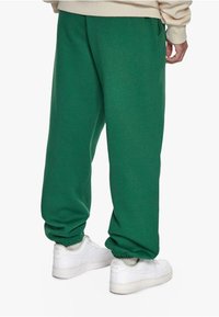 Grüne Sweatpants mit einem elastischen Bund und Bündchen. Hergestellt aus einem weichen Stoff, mit seitlichen Taschen. Kombiniert mit weißen Sneakern.