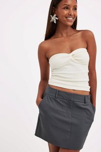 Valkoinen ribbi-hihaton toppi, jossa on kierretty etuosa, yhdistettynä harmaaseen räätälöityyn mini-hameeseen, jossa on sivutaskut ja sileä kangas.