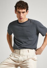Camiseta a rayas en tonos navy con cuello redondo y mangas cortas, combinada con pantalones pleated de un beige claro. La tela tiene una textura suave.