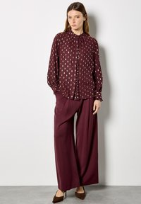 Burgundy blouse with pleated details and leaf patterns, paired with wide-leg trousers. Silk-like fabric with a smooth texture. Brown heels.