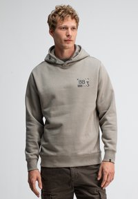 Lichtgrijze hoodie met een logo aan de voorkant, een trekkoord en geribbelde boorden. Zachte stof, casual pasvorm, geschikt voor layering.