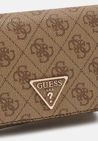Brun teksturert lommebok med preget mønster, med en gyllen trekantet logoplater som viser "GUESS USA." Kompakt design med subtil detailing.