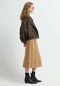 Bruine houndstooth cropped jack met grote knopen, gecombineerd met een geplooide beige midi-rok en zwarte enkelboots met spitse neuzen.