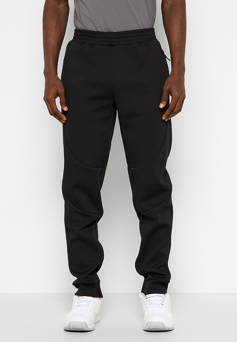 Joggers noirs ajustés avec un tissu texturé et une taille élastique. Comprend des poches latérales et des détails de panneaux courbés. Associés à des baskets blanches.