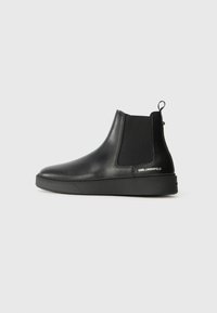 Botas Chelsea de cuero negro con paneles elásticos laterales y una suela de goma gruesa. Cuenta con una pestaña de tirón y un detalle de la marca en el talón.