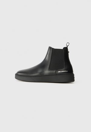 Black leather Chelsea boots with elastic side panels and a thick rubber sole. Features a pull tab and branded detail on the heel.