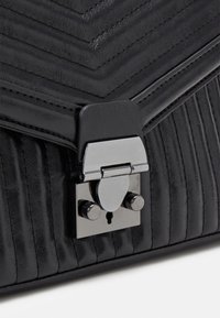 Bolso de piel negra con un diseño acolchado, que presenta un cierre y herrajes en tono plateado, y una textura acanalada vertical en el panel frontal.