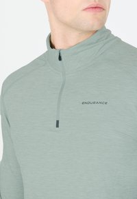 Lichtgroene sportpullover met een kwart-rits kraag, gemaakt van een textuurstof. Kenmerkt zich door de "ENDURANCE" branding in donkergrijs op de borst.