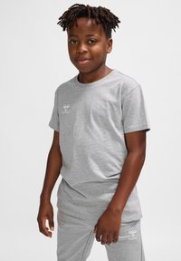 Grå bomulds t-shirt med korte ærmer, rund halsudskæring og et lille hvidt logo på brystet, parret med grå bukser.