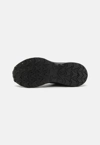 Semelle de chaussure en caoutchouc noir avec un motif de bande de roulement texturé, présentant des rainures angulaires et des éléments surélevés pour une traction et une adhérence.