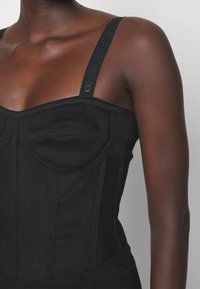 Svart korsett-topp med strukturerade kupor, sidsömmar och breda axelremmar med präglad logotyp. Slät textur och skräddarsydd passform.