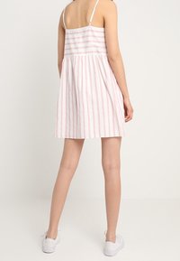 Un vestido de tirantes a rayas en rosa claro y blanco, con un corsé ajustado, tirantes ajustables y una falda acampanada que llega por encima de las rodillas.