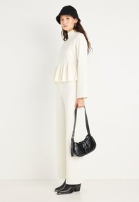 Top peplum crema con maniche lunghe, abbinato a pantaloni wide-leg coordinati. Una borsa a tracolla in pelle nera e stivali con punta a tronchetto completano l'outfit.