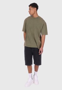 Oliven grøn oversized t-shirt i bomuldsstof, parret med sorte denimshorts. Hvide sneakers og ankelsokker fuldender outfittet.
