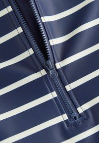 Tissu rayé bleu marine et crème avec un détail de fermeture éclair. Texture lisse, conception mi-longue et motif rayé contrastant.