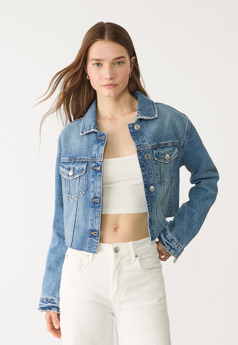 Jeans jakna s svetlo modrim pranjem, z ovratnikom, sprednjimi žepi in srebrno kovinsko opremo. Zasnovana je s skrajšanim krojem in dolgimi rokavi.