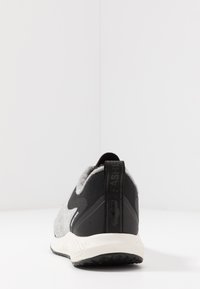 Baskets en tissu gris avec un dos et une semelle en synthétique noir. Présentent un motif texturé et une languette avec une marque au niveau du talon.