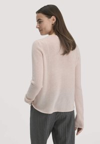 Rosa langer Pullover mit langen Ärmeln und lockerer Passform, ausgestattet mit rundem Halsausschnitt und geripptem Saum, kombiniert mit grauen gestreiften Hosen.