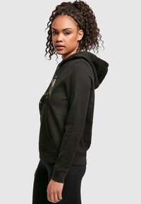 Svart hoodie med framficka, dragsko i huven och grafisk tryck på bröstet. Mjuk tyg med avslappnad passform och ribbade ärmslut.