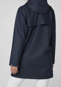 Imperméable bleu marine en matériau lisse et imperméable, avec capuche, poignets à boutons, et une pièce arrière plus longue pour une meilleure couverture.