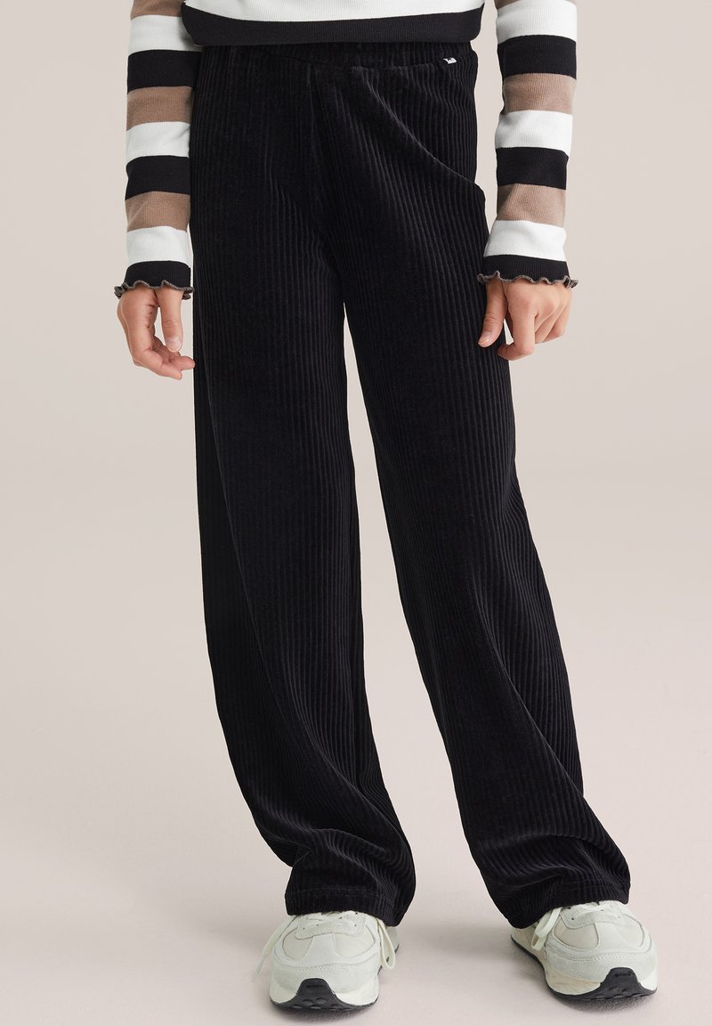 Čierne kordúrové nohavice s širokými nohavicami a ribbovanou textúrou, s uvoľneným strihom a elastickým pásom. Skombinované s svetlými teniskami.