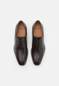 Chaussures habillées en cuir noir au design élégant, avec un bout pointu, cinq œillets pour les lacets et une texture lisse.
