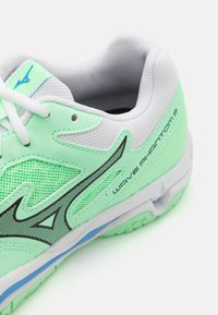 Hellgrüner Sportschuh mit weißen Akzenten, Mesh-Obermaterial und schwarzen Details. Verfügt über eine strukturierte Oberfläche und ein Logo an der Seite.