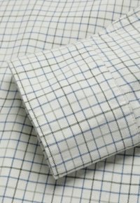 Camisa de algodón con un tejido blanco y patrones de cuadrícula en azul y verde. Textura suave con un puño doblado que muestra el mismo patrón.