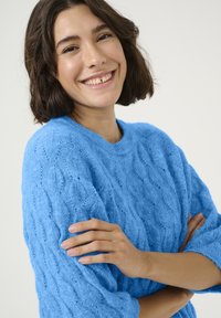 Világoskék kötött pulóver, kábelmintával, kerek nyakkal és háromnegyedes ujjakkal. Puha tapintású és laza fazonú.