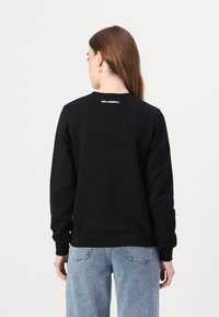 Sort sweatshirt lavet af tykt stof. Har en rund halsudskæring og et lille hvidt logo på den øverste del af ryggen. Blevet parret med lyseblå denim.