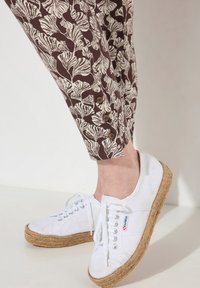 Pantaloni marroni con un motivo floreale bianco, caratterizzati da bottoni marroni all'orlo. Abbinati a sneakers bianche con suola in iuta.