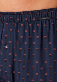 Marineblauwe boxers met rode en zwarte verticale strepen, voorzien van een knoopsluiting en een elastische tailleband, gemaakt van zacht katoen.