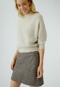 Un pull côtelé beige clair avec un col montant, associé à une jupe courte en vichy noir et blanc. Texture douce et coupe décontractée.