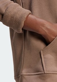 Brun sweatshirt med texturerad mudd, mjukt tyg och detalj med framficka. Materialet har en slät yta med synliga sömmar.